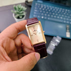Elegant Franklord Champagne Gold watch with gold dial and maroon strap held in hand
