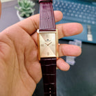 Close-up of Franklord Champagne Gold watch with rose gold rectangular dial and maroon leather strap