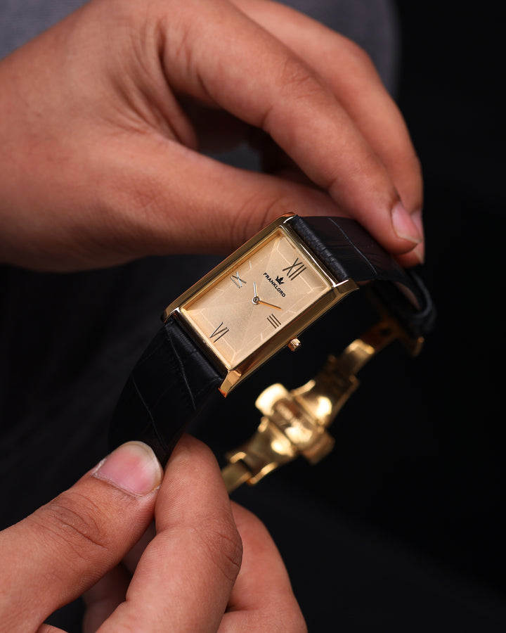 Close-up handheld shot of Franklord Royal Gold Heritage rectangular watch with gold dial and black strap