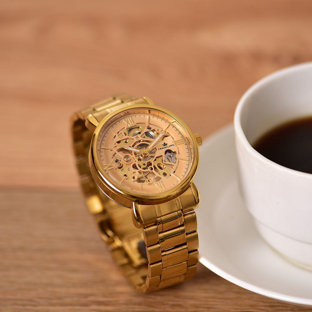 Franklord Mechanis Regal Gold Watch standing upright next to a cup of coffee, emphasizing its luxurious gold design and sophisticated craftsmanship.