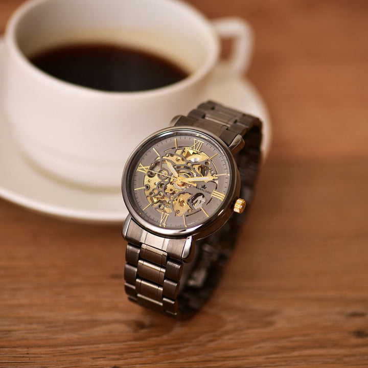 Franklord Titanium Shadow Watch elegantly placed next to a cup of coffee on a wooden surface, showcasing its modern skeleton dial and titanium finish.